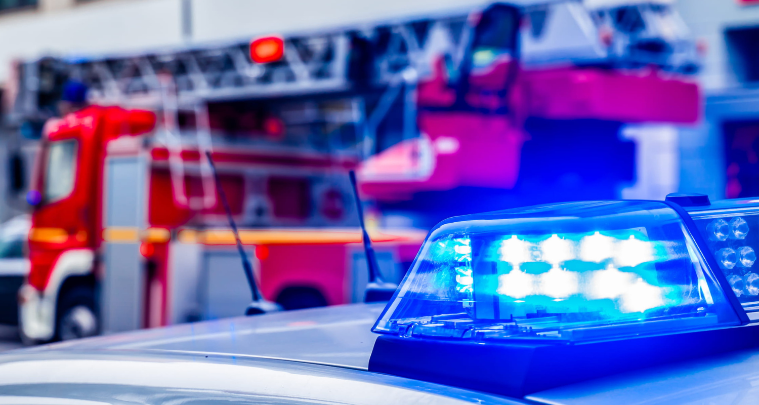 Blue police vehicle lights with fire trucks in the background, representing upfitted first responder units